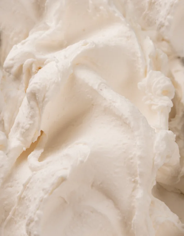 Close-up of a creamy white whipped mixture with soft swirls and peaks, like frosting or whipped cream.