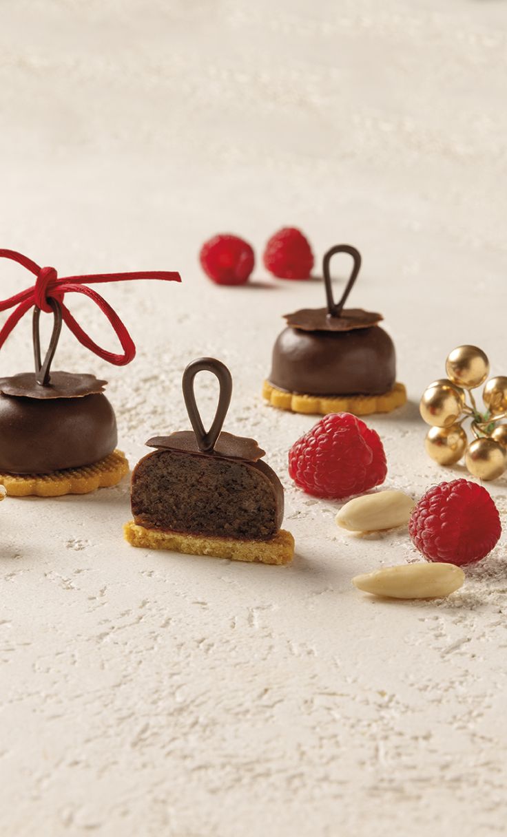 Dolcetti al cioccolato su base di biscotto, uno tagliato, con lamponi, mandorle e nastro rosso.
