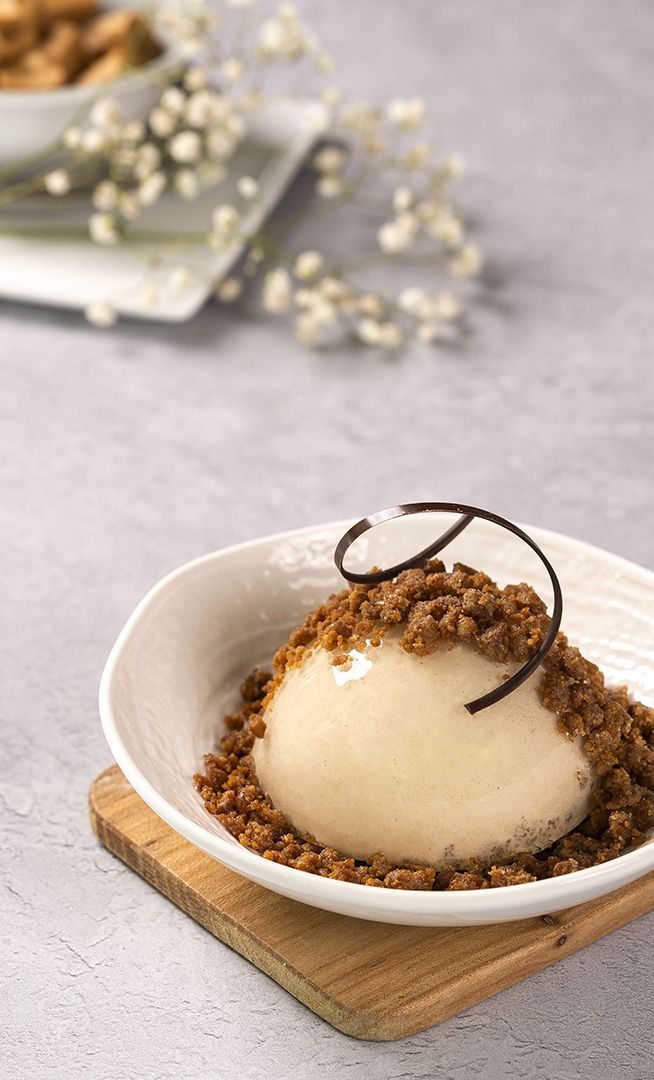 Gelato alla vaniglia in ciotola bianca con crumble e ricciolo di cioccolato su tagliere di legno